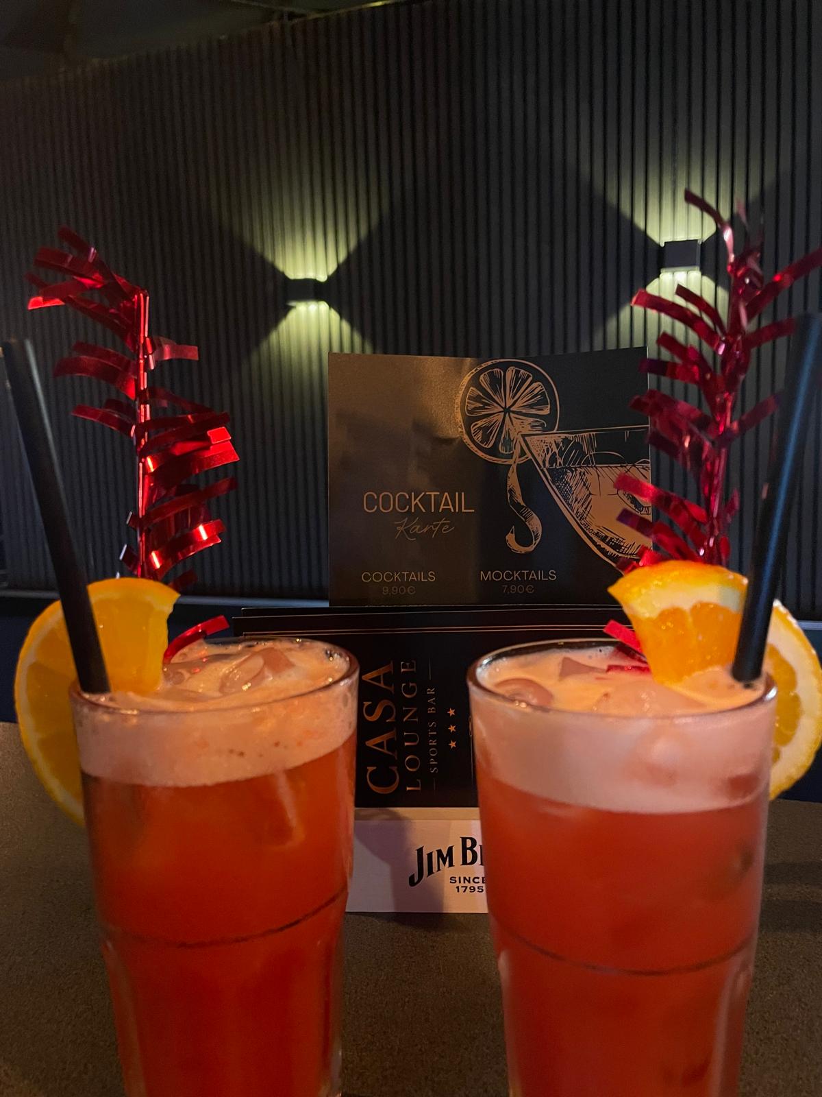Zwei hausgemachte Cocktails mit Orangenscheiben vor der Cocktailkarte der Casa Lounge