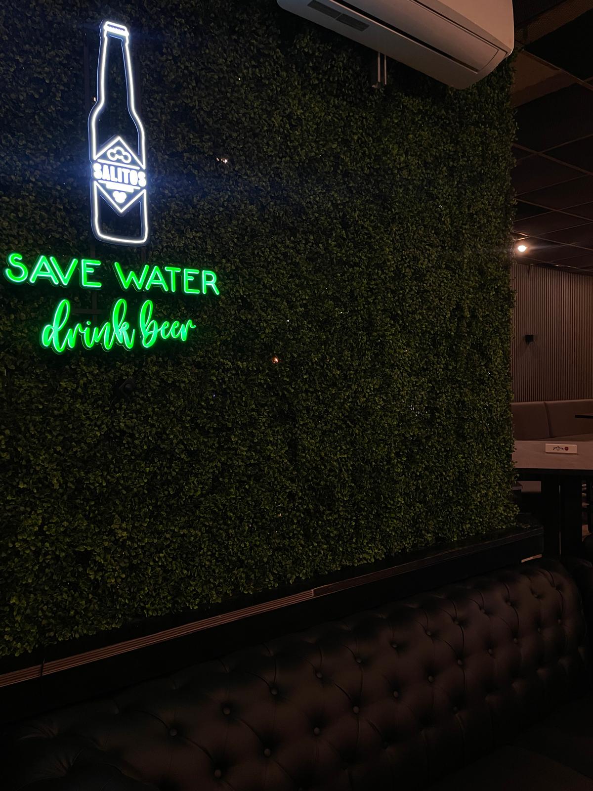 Lounge-Ecke mit Chesterfield-Sofa vor grüner Pflanzenwand und Neon-Schriftzug