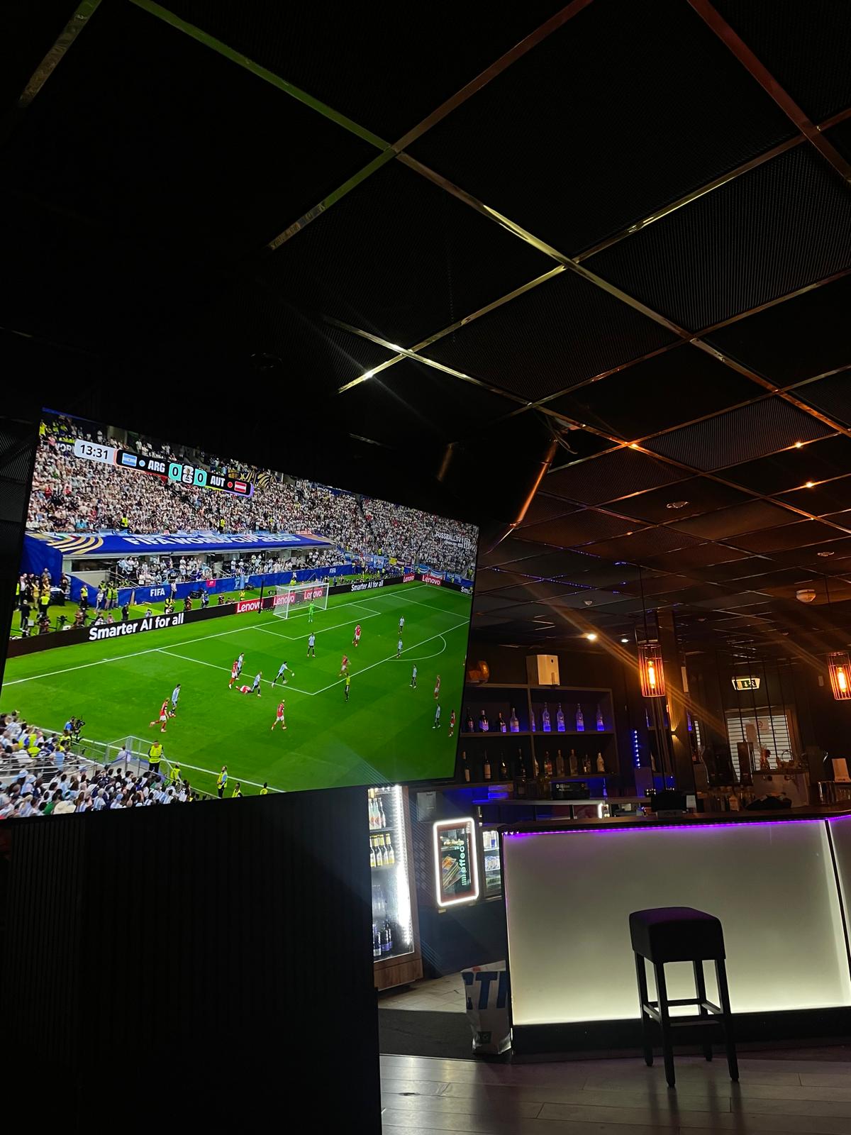 Fußball-Übertragung auf großem Screen über der beleuchteten Bar